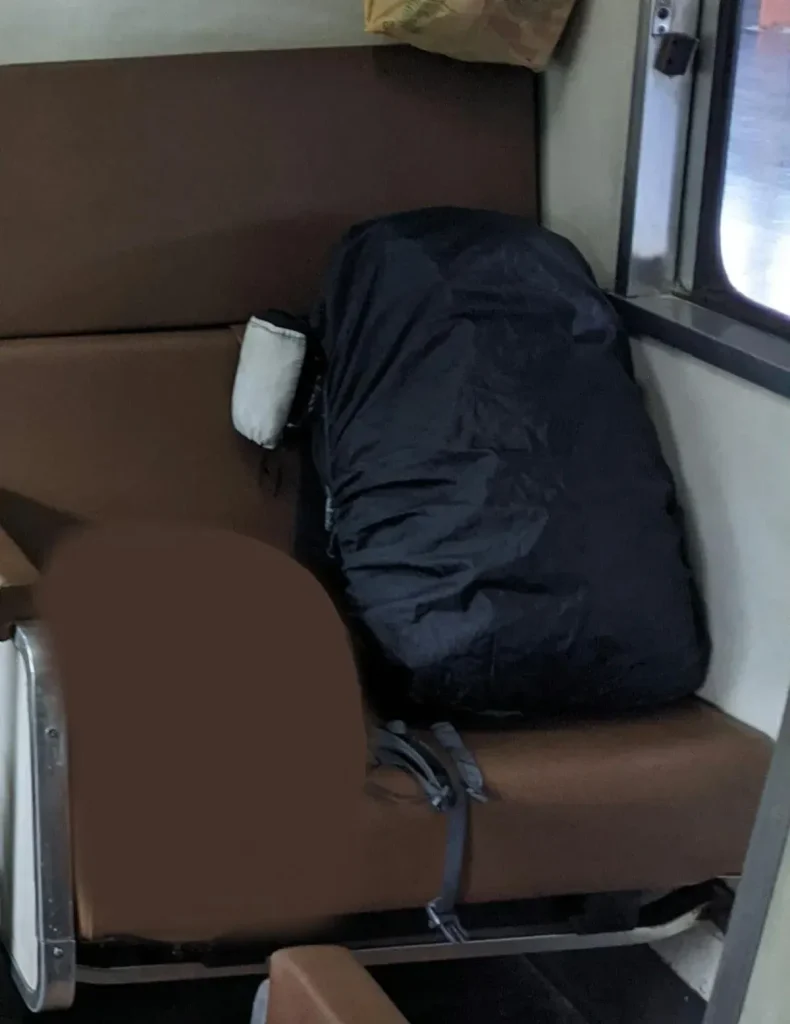 Carryon-sized 30 liter backpack (a.k.a in-cabin baggage) resting within a passenger's train seat. It has a rain cover over it that has an elastic band around it's permiter - good for stuffing things inside (between the bag and the rain cover), preventing theft. The rain cover, per the name, protects against water as it is made of water-resistant material.