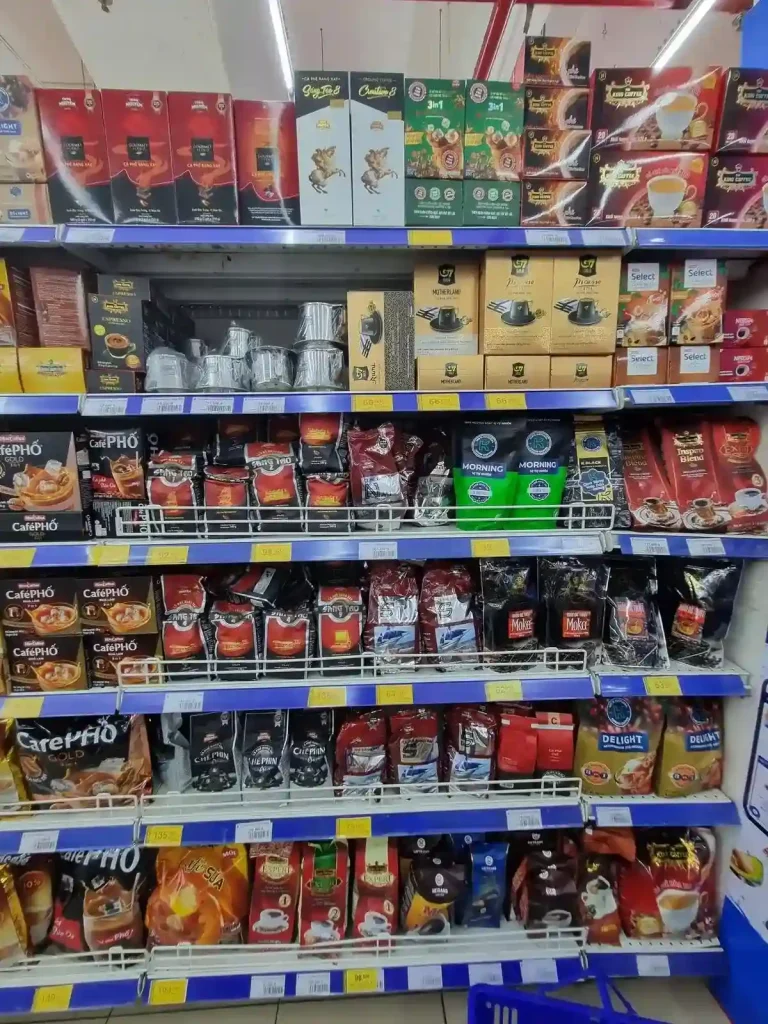 A grocery isle of Vietnamese coffee bean brands in Vietnam. The aisle also has a Vietnamese phin brewing filter for sale.
