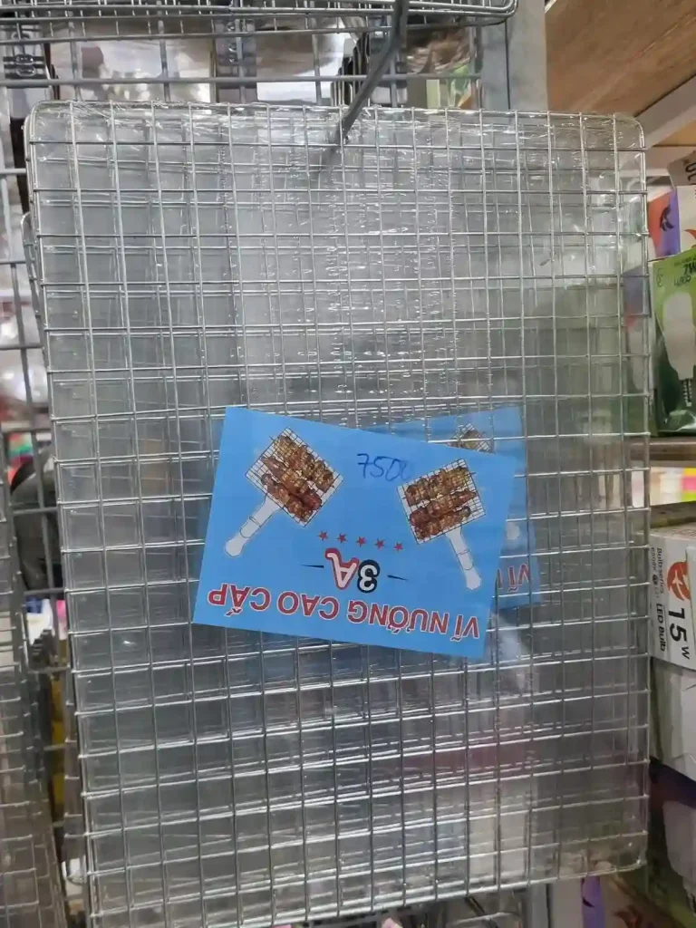 Grill plate to grill food on. A rectangular grill plate made of wire in which juice can drip through (not a solid plate like sheet metal). It is rectangular and long. It is at a shop in Southeast Asia.
