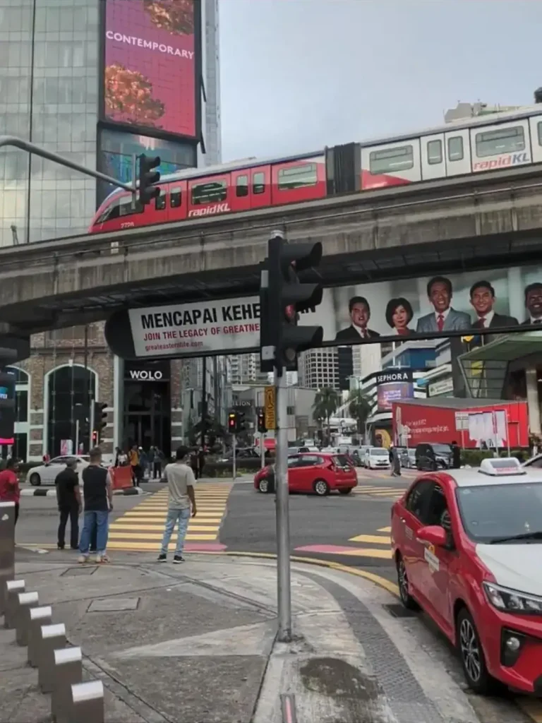 An image depicting busy big city life. The location is in Kula Lumpur, Malaysia. Public transportation in the form of elevated metro line (a.k.a subway or tube) is center in this image.