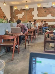 A man working at café with a laptop on a desk and seating. This represents a place to work from for remote workers in Southeast Asia.