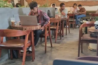A man working at café with a laptop on a desk and seating. This represents a place to work from for remote workers in Southeast Asia.