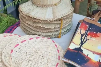 A table of artisan souvenirs in Cambodia; including a straw hat, hand-waved air fan, and tote bags with various motifs printed on them of local surrounding such as from within Angkor Watt Park.