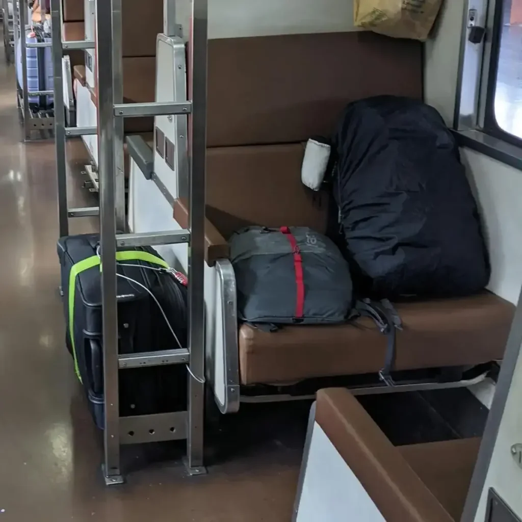 2 carry-on travel bags - one small and one medium sized - and a check-in luggage bag. The 2 check-in bags are on a seat on a train, and the check-in luggage bag is on a storage rack next to the seat. This picture conveys the different sizes of the travel bags.