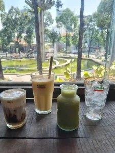 An image of a three drinks and a water on a table in a café in Vietnam called Cong Cafe. Drinks include a coffee, a smoothie, and a juice.