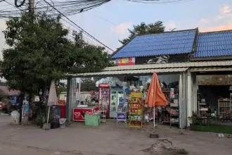 A local family-owned "mom and pop" convenience store in Cambodia. This is very common all throughout Cambodia and Southeast Asia, in general. Located on a street corner, the store has not walls on the two sides that face the street. Inside, the store has two refrigerators with drinks, a deep freezer with ice cream, and racks with various snack food on them. A corrugated sheet metal roof covers the store.