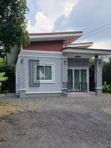 A small modern house in Southeast Asia, representative of a common home building style. It is made of concrete, has a covered front porch, and a gravel driveway.