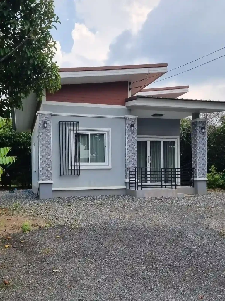 A small modern house in Southeast Asia, representative of a common home building style. It is made of concrete, has a covered front porch, and a gravel driveway.