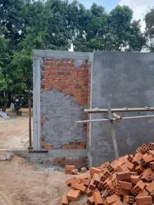 An image showing the construction method in Southeast Asia for building homes. This is a wall around home still under construction. It is brick laid to construct a wall, then concrete is smeared over it and smoothed out.