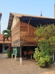 A traditional wooden house in Southeast Asia. The home is a stilt house, meaning it is elevated off of the ground (this one is elevated about five feet off the dirt ground). Below is empty, but often used for storage. The house is framed using wood, and the stilts are vertical wooden beams driven into the ground. The roof is corrugated steel sheet.