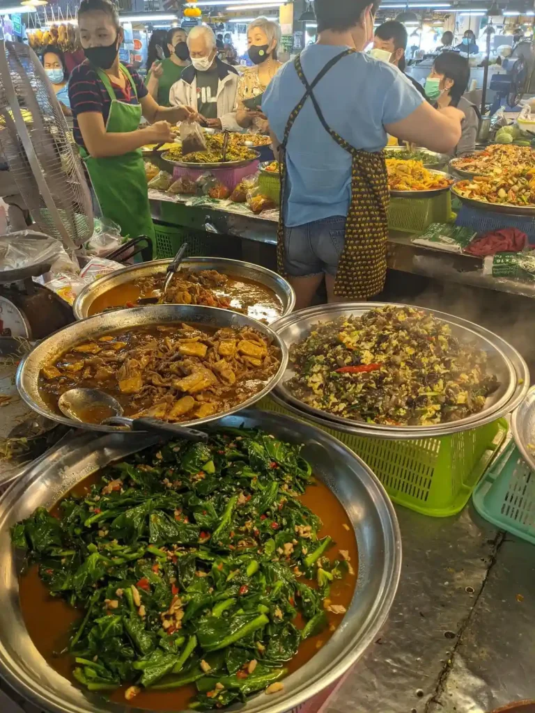 Several pre-cooked food dishes being sold at an indoor food market in Thailand. The food, is of course, Thai food.