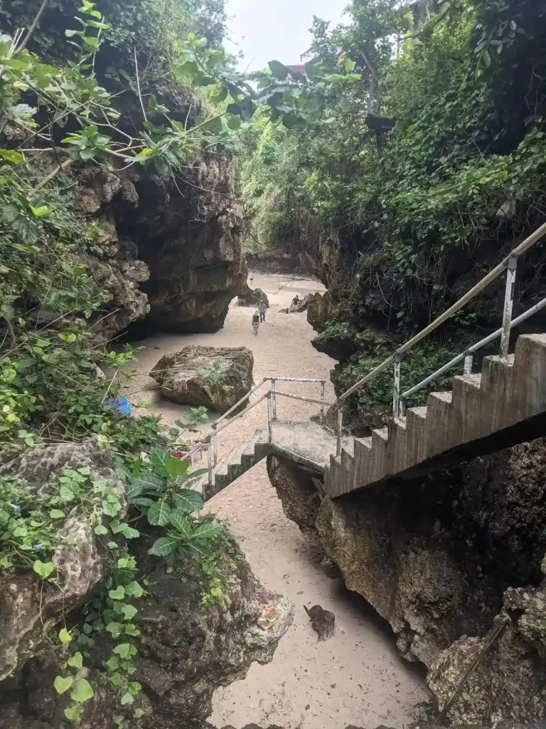 A crevice area, whose ground is filled with sand. The crevice leads to a beach.