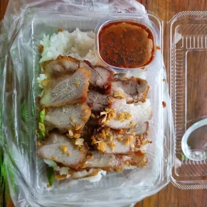 A portion of Thai crispy pork on white rice with a sauce, packaged to take home.
