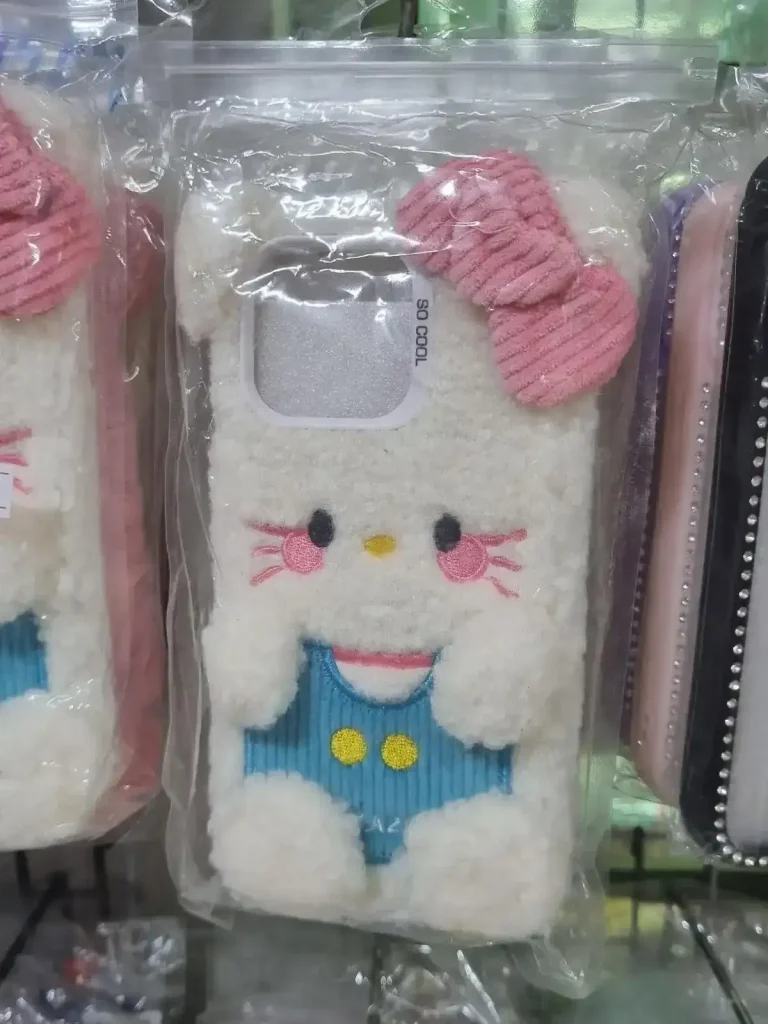 iPhone phone case. A phone cute case with fur on it for iPhone sold in Southeast Asia. It is a fury cat with a blue shirt on, four puffy balls stuck onto the case to represent paws, a pink bowtie in the upper right-had corner, and two puffy balls stuck on the case to represent ears in the upper left & right-hand corners.