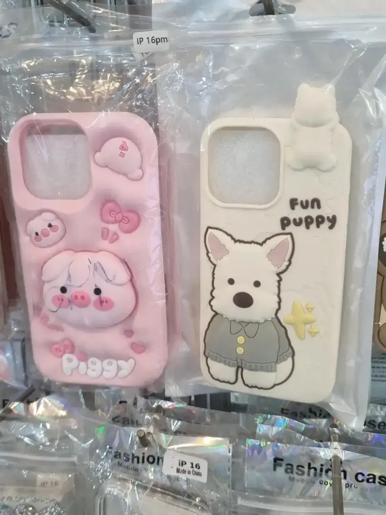iPhone phone case. Two cute phone cases for iPhone sold in Southeast Asia. One is pink with a two faces of a pig and the bubbly rear side of a pig, and says "Piggy" on it. The other is a poodle dog with clothing and a bow tie that says "Fun Puppy" on it.