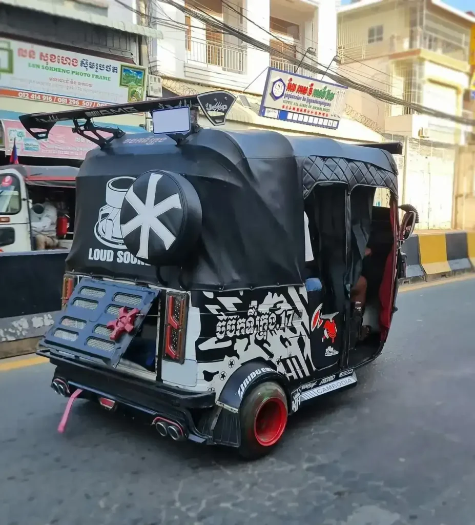 A Bajaj Indian-style tuk-tuk in Cambodia. It is three wheeled and is fully enclosed. This tuk-tuk is decorated with various visual graphics per the owner/driver's amusement, which is a common thing to do in Cambodia.