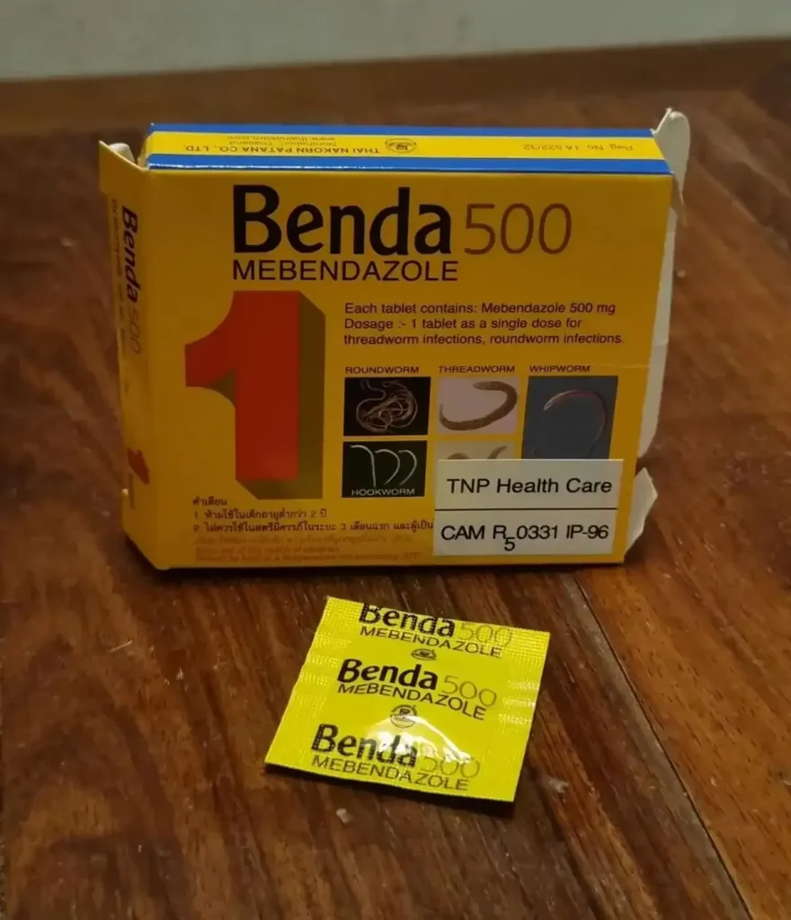 An image of a one-pill box of Mebendazole, along with the pill taken out of the box. This is a medicinal pill to treat for parasitic worm infections. In Southeast Asia, it is commonly taken to ensure that the body stays clear of parasitic worms.