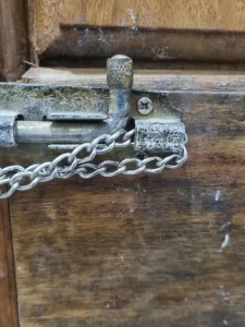 A close-up of a small-linked chain that is fed through a hole in a door latch. Not show is how it also feeds through the latch mounted on the door frame on the wall. This ties the door to the door frame. A small TSA four pin travel lock (also not shown in this image) connects & locks both ends of the chain together. This means that the door cannot be opened until the lock & chain are taken off.