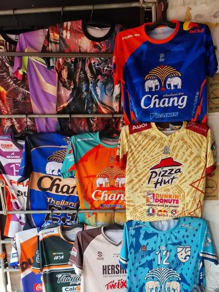 An assortment of dry-fit t-shirts or jerseys at store in Thailand. Some shirts have the Chang beverage company logo on them, which is well known for producing Change beer. Others have the Pizza Hut logo, Hershey logo, and various other prints.