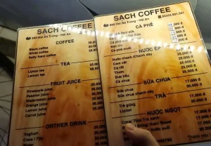 Two menus at a café in Vietnam, one for locals (written in Vietnamese) and one for foreigners (written in English). The menus have different pricing, where the foreigner menu pays more. The foreigner menu costs thirty thousand Viet Dong for a "Black coffee", while it's Vietnamese-written counterpart "Ca phe den" (coffee black) costs eighteen thousand Viet Dong. That is a forty percent increase for being foreign. A can of Coca Cola is twenty thousand for foreigners versus seventeen thousand for locals.