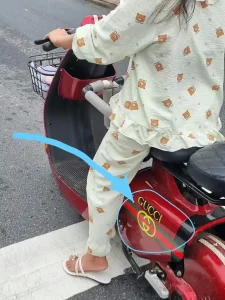 A feamle riding a small electric scooter with fake Gucci branding in Vietnam.