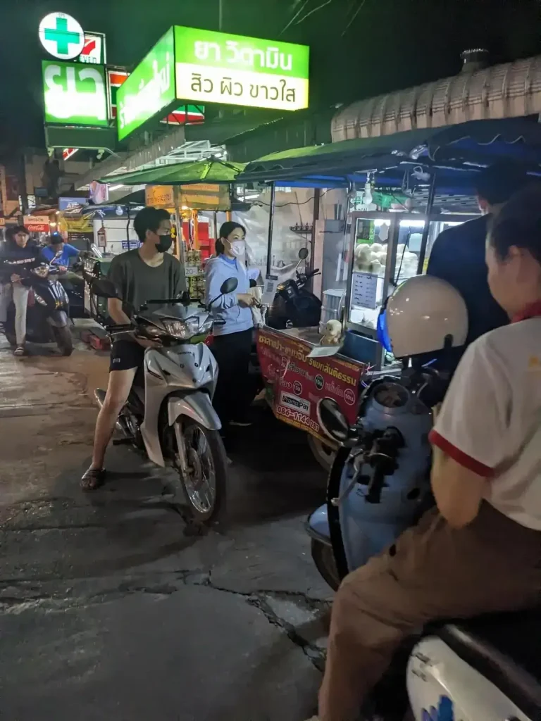 Food stalls along a small street at night in Thailand. People park their motorbikes (scooters) next to the food stalls to order foor to-go.
