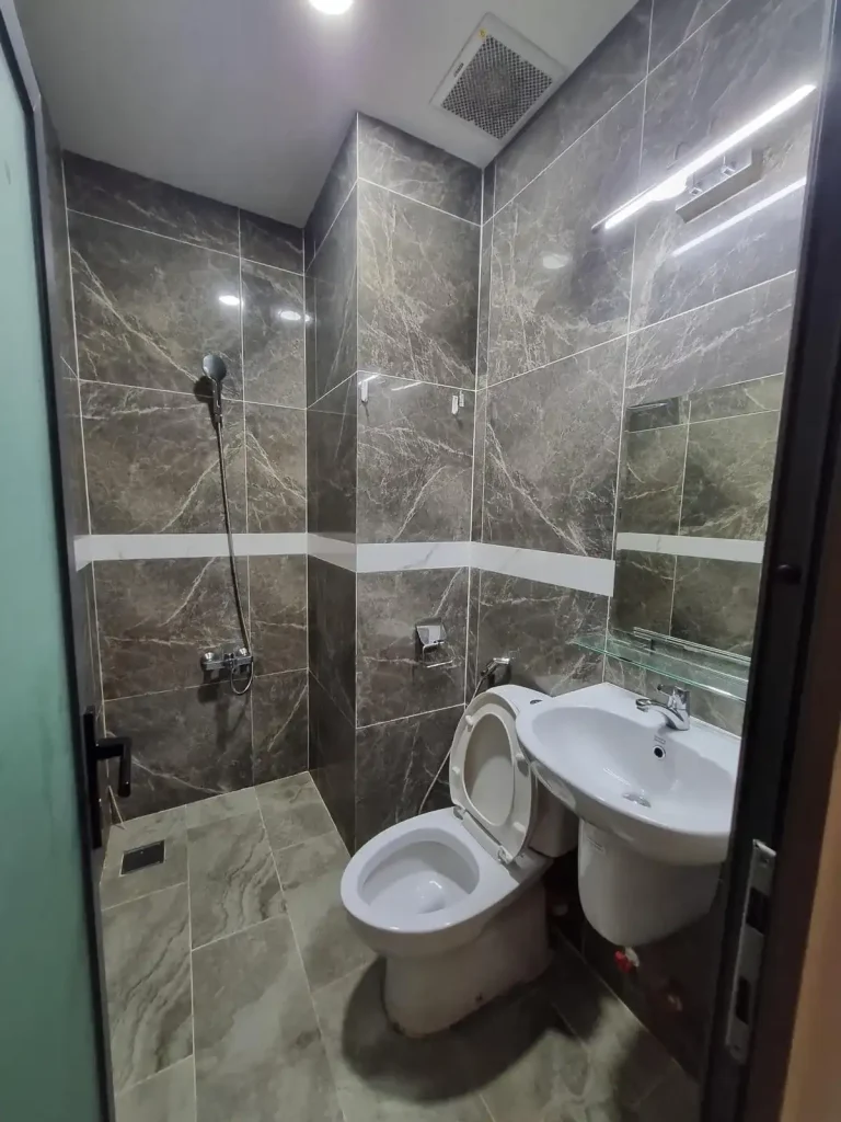 The bathroom of a fully furnished studio room rented monthly in Southeast Asia. The image shows a "wet bathroom", which is the style in Southeast Asia in which there is no divider between the shower and sink & toilet. The flooring is tile, and water from the shower can splash anywhere within the bathroom.