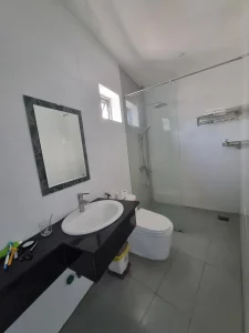The bathroom of a furnished hotel room in Southeast Asia without a kitchen. It has a partial divider between the shower and toilet & sink area. A "wet bathroom" is the most common style in Southeast Asia in which there is no divider between the shower and sink & toilet. The flooring is tile, and water from the shower can splash anywhere within the bathroom.