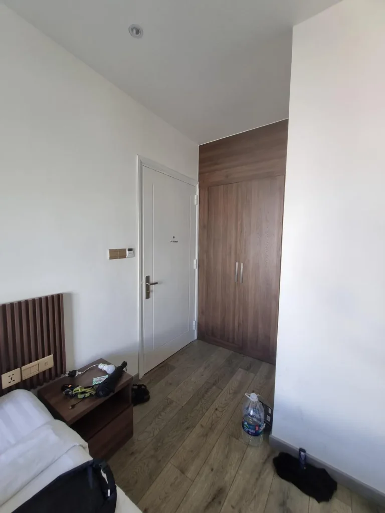 The wardrobe storage area that is building into the wall near the door entrance. This is within a furnished hotel room in Southeast Asia without a kitchen.