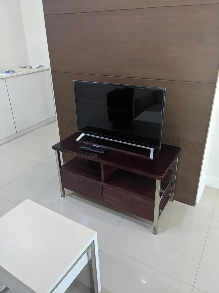 An image showing a television on an entertainment center located in the family room of a furnished one bedroom apartment that is rented monthly in Southeast Asia. The floor is tile, which is very common in Southeast Asia.