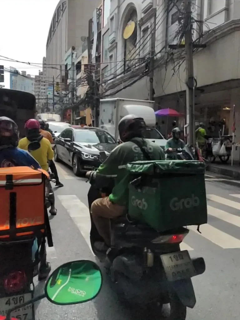 Grab ridehailing food delivery. A delivery man riding down the road on a scooter with a basket on the back for delivering food and drinks in Southeast Asia. The basket has the company's name on it, "Grab", and logo.
