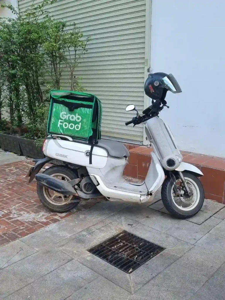 Grab ridehailing food delivery. A parked scooter with a basket on the back for delivering food and drinks in Southeast Asia. The basket has the company's name on it, "Grab", and logo.