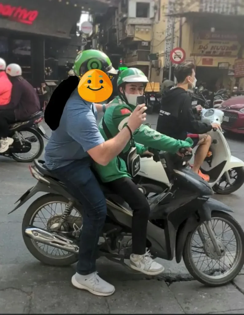 A passenger on the back of a motorbike taxi, booking through the Grab ride hailing smart phone application.