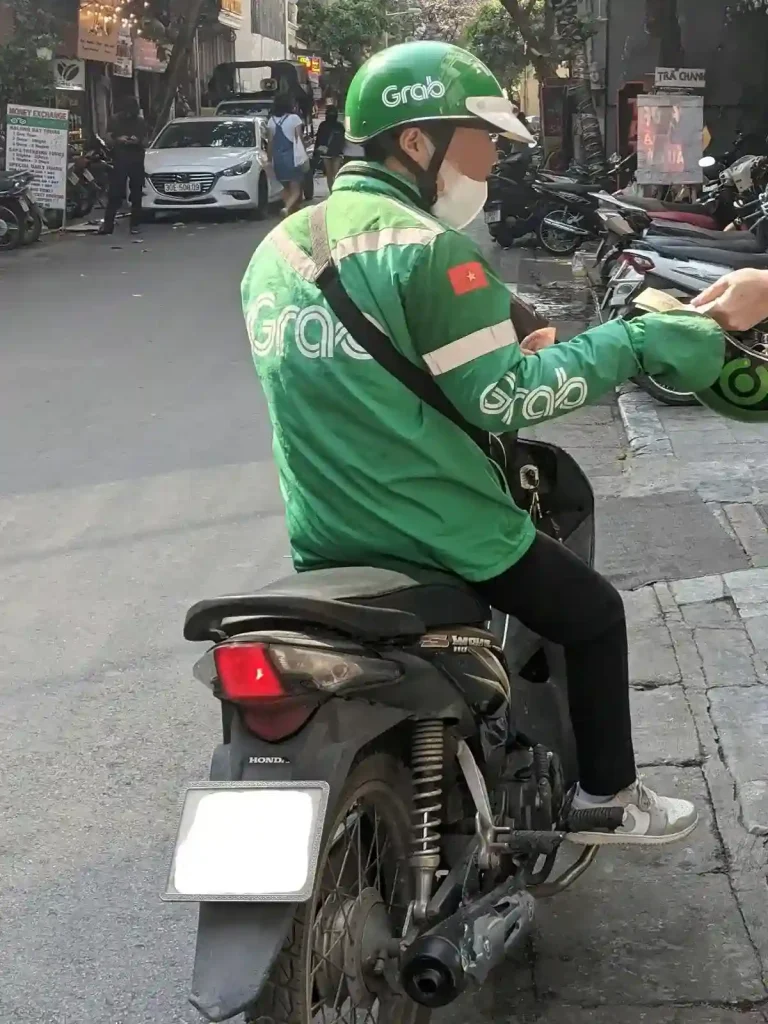 A driver of a motorbike taxi on his motorbike. He is employed through the Grab ride hailing company, and is wearing Grab-branded helmet and jacket.