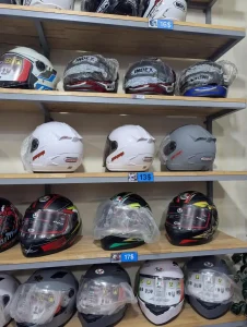 Helmets of various styles at a helmet shop in Southeast Asia. The helmets in this image are sporty, and covers the chin for full-face coverage. The helmets also have a face shield feature that can be pulled downward (to use the face shield) or upward (to get rid of the shield). Price is thirteen US dollars, and others are sixteen or seventeen US dollars.