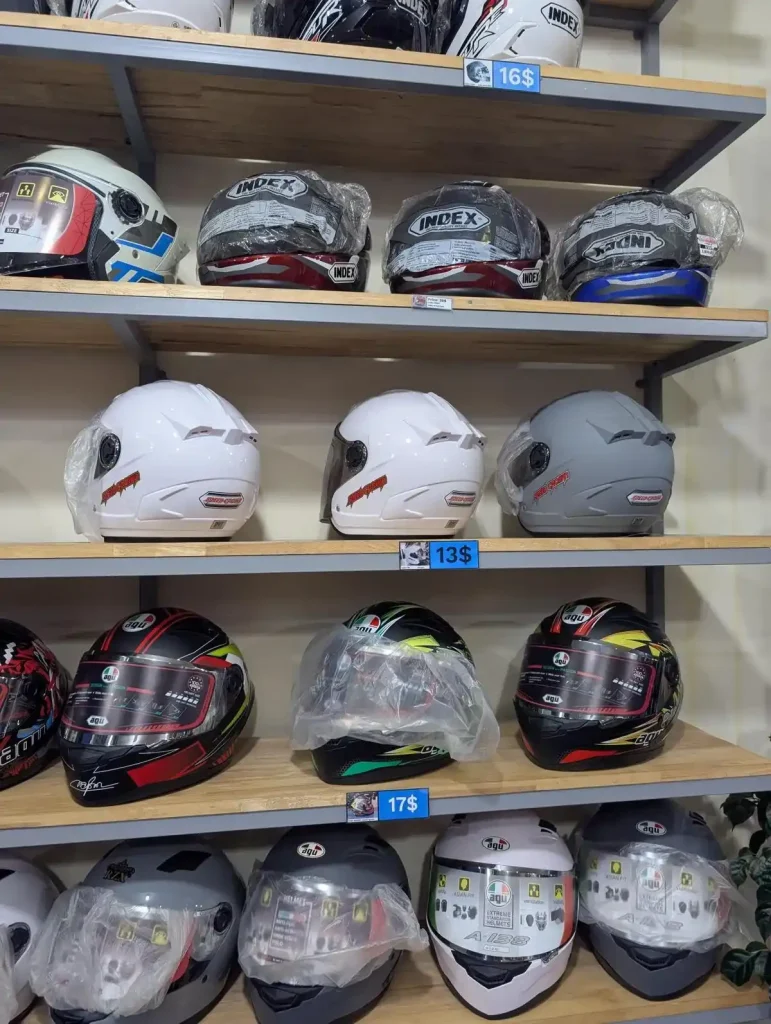 Helmets of various styles at a helmet shop in Southeast Asia. The helmets in this image are sporty, and covers the chin for full-face coverage. The helmets also have a face shield feature that can be pulled downward (to use the face shield) or upward (to get rid of the shield). Price is thirteen US dollars, and others are sixteen or seventeen US dollars.