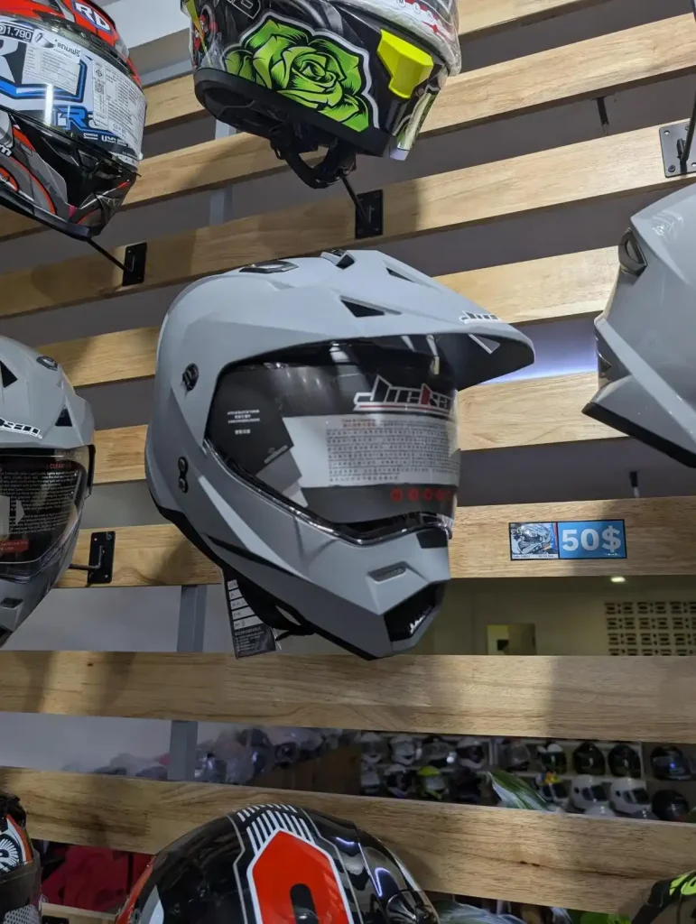 Helmets of various styles at a helmet shop in Southeast Asia. The helmets in this image are sporty. They have a hat-style cover to block the sun, and the helmet covers the chin for full-face coverage. The helmets also have a face shield feature that can be pulled downward (to use the face shield) or upward (to get rid of the shield). Price is fifty US dollars.