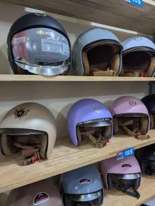 Helmets of various styles at a helmet shop in Southeast Asia. The helmet in the image have a face shield feature that can be pulled downward (to use the face shield) or upward (to get rid of the shield). There is no chin coverage (i.e. it is not a full-face-covered helmet). Price is eighteen US dollars.