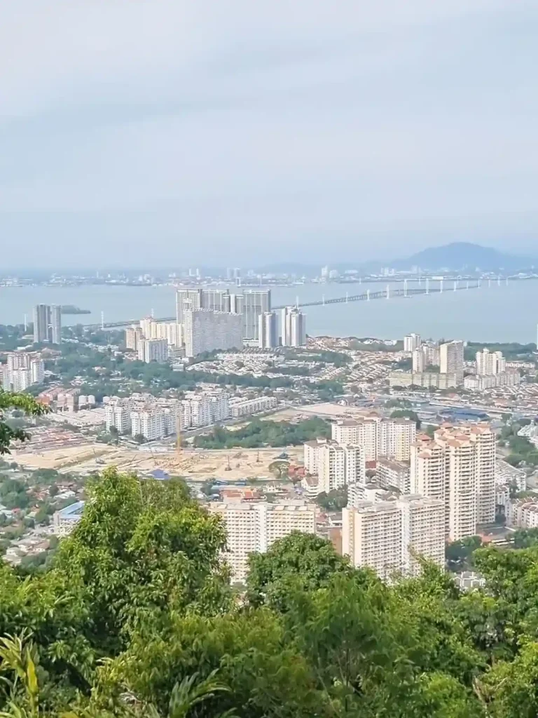 A hiking viewpoint on Penang Island, Malaysia showing several high rises, the ocean bay and a bridge that goes between the island and mainland.