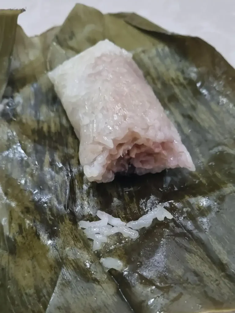 A steamed gluttonous sticky rice covered banana snacks with the banana leaf removed. A bite has been bitten into it, showing the banana in the middle, and wrapped with sticky rice.