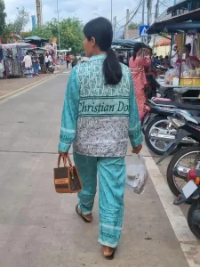 A female wearing a set of knock-off Christian Dior pajamas, walking down the street in Cambodia.