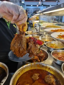A lamb shank being shown to the photographer of this image by the Indian worker at an Indian-Malaysian restaurant called a Mamak or Nasi Kandar.