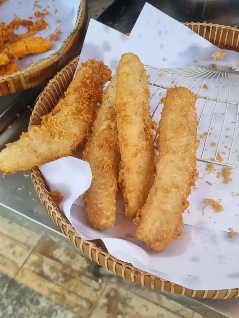 Deep fried bananas in a basket for sale in Cambodia, the long and flat variant. This is a common snack throughout Southeast Asia. Bananas are peeled, sliced, covered in a battered, and then deep fried. Deep fried bananas come in a few different variations. The ones in this image are the long and flat version.