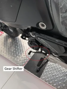 An image of a manual motorcycle. There is text with arrows pointing at the controls of a manual motorcycle. This image highlights the location of the gear shifter.