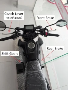 An image of a manual motorcycle. There is text with arrows pointing at the controls of a manual motorcycle. This image highlights the locations of the clutch lever (to shift gear), gear shifter, front brake, and rear brake.