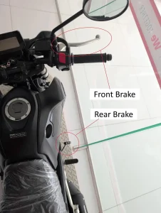 An image of a manual motorcycle. There is text with arrows pointing at the controls of a manual motorcycle. This image highlights the locations of the front brake and rear brake.