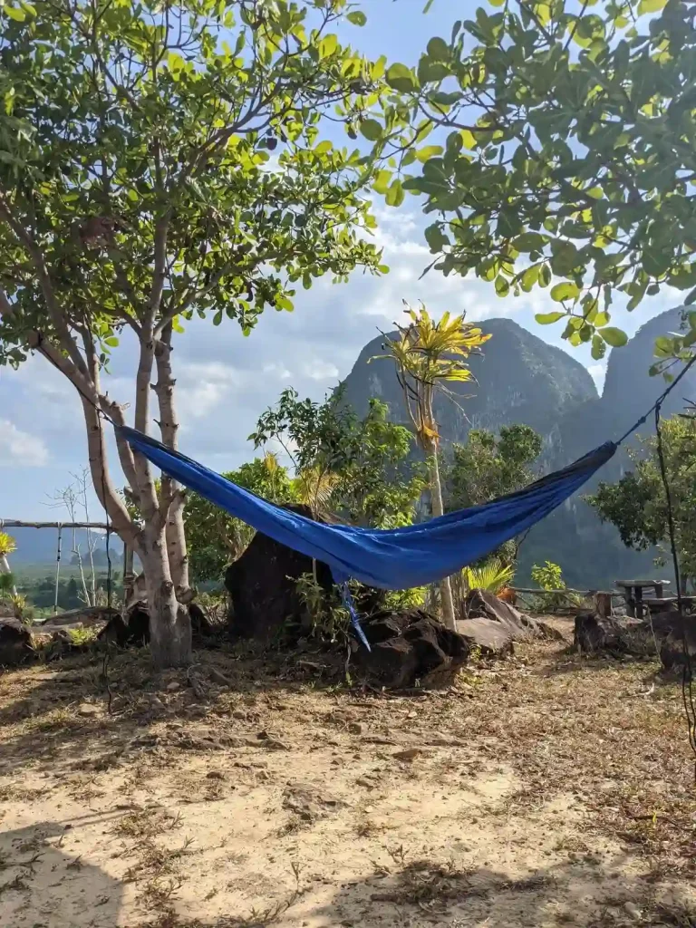 Hammock camping within a section of trees at a camping spot. Rounded mountains are in the background. This is a camping spot is located at Kuan Nom Saow Restaurant and Viewpoint in Krabi Thailand.
