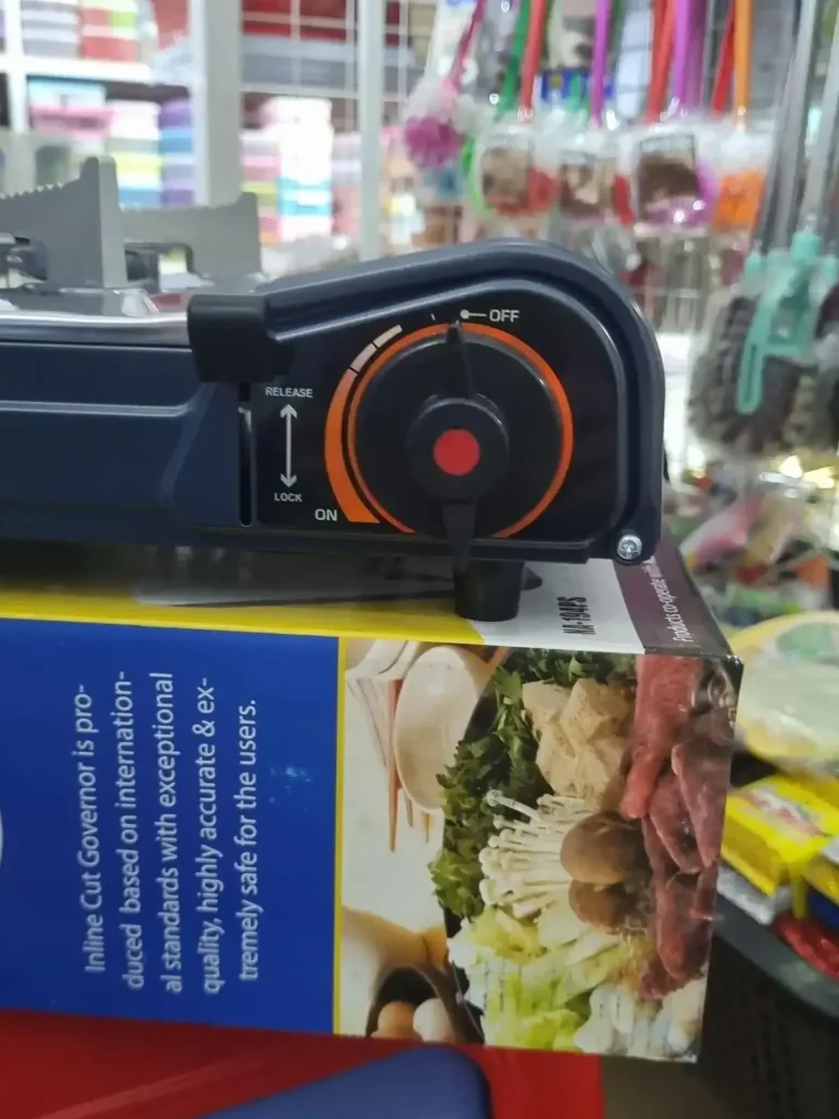 A close-up view of the on/off controll switch that controls the flame on a portable gas cooker for sale in a store in Southeast Asia. This on/off switch is variable - by twisting it between off and on, the strength (and thus heat) of the flame can be adjusted. When the switch is pointing to "ON" the flame will be at full-blast (i.e. the strongest and hotest) settting that the cooker can do. There is also a clamp to "Release or Lock" the gas canister into the stove cooker.