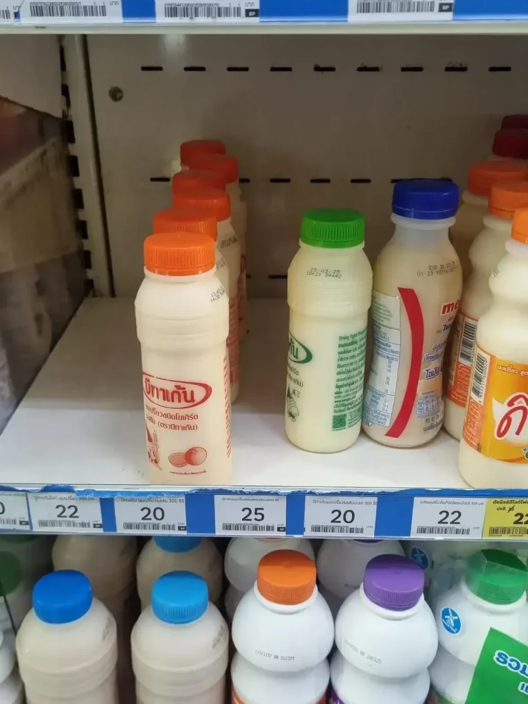 A medium bottle of probiotic drink on a convenience store shelf in Thailand priced at roughly seventy US cents (22 Thai baht). Flavors shown are orange and green-colored bottle of unknown flavor. This is good to drink when you have an upset stomach or diarrhea.