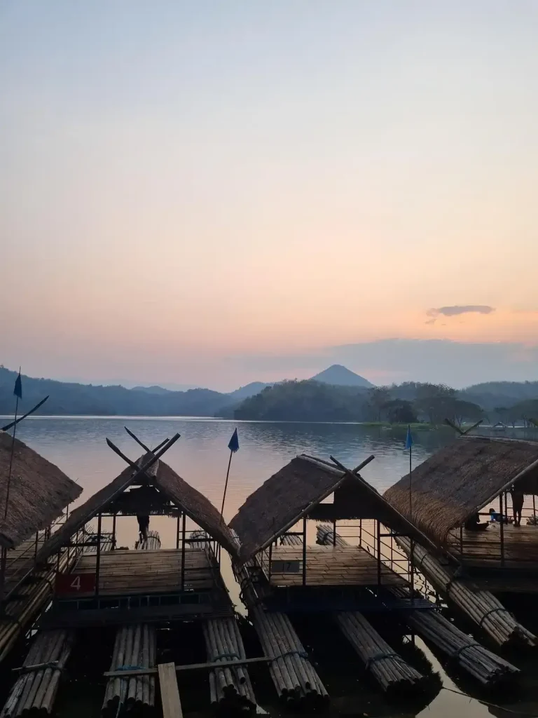 Several bamboo rafts along the shore of a lake in Thailand. It is sunset and no-one is in sight. These rafts are large enough for eight people and are have a roof over the seating area. They are towed out into the middle of the lake, and food is served to the patrons on the rafts. This is unique concept of a restaurant.
